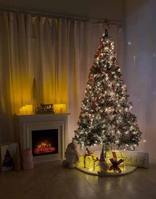 Modern silver Christmas set at La Vie Rental Studio Clearwater FL — frosted flocked tree with gold star, white mantel with candles and Merry Christmas sign, glowing gift boxes and gnome on sheer-curtain backdrop